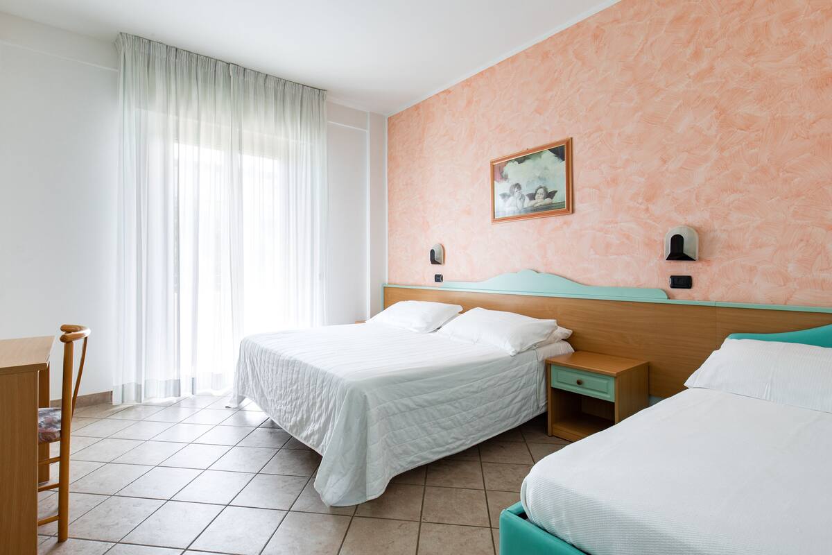 Una camera d'albergo con due letti, una scrivania e una sedia.