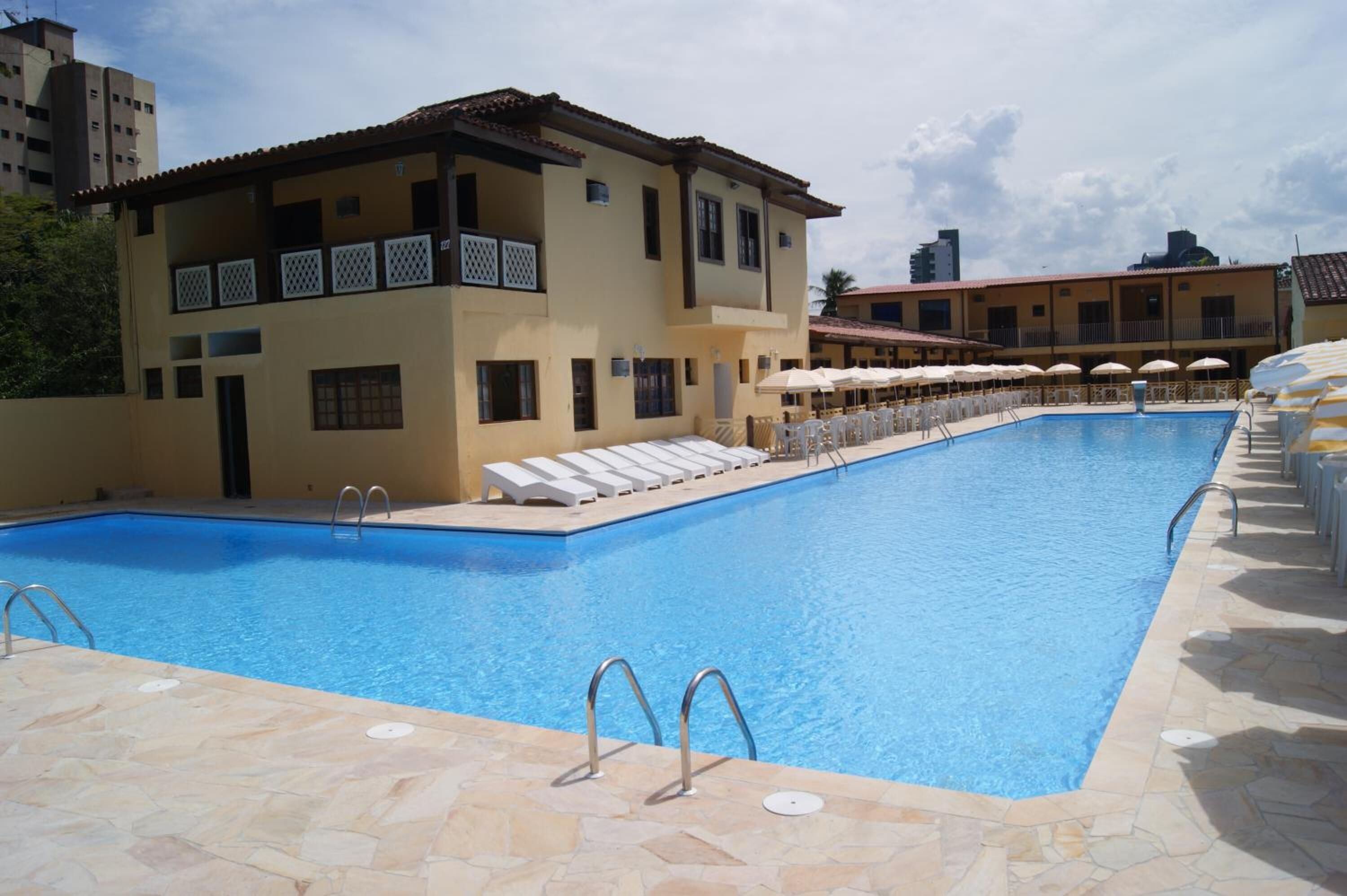 A swimming pool with sun loungers and umbrellas, surrounded by buildings with balconies.