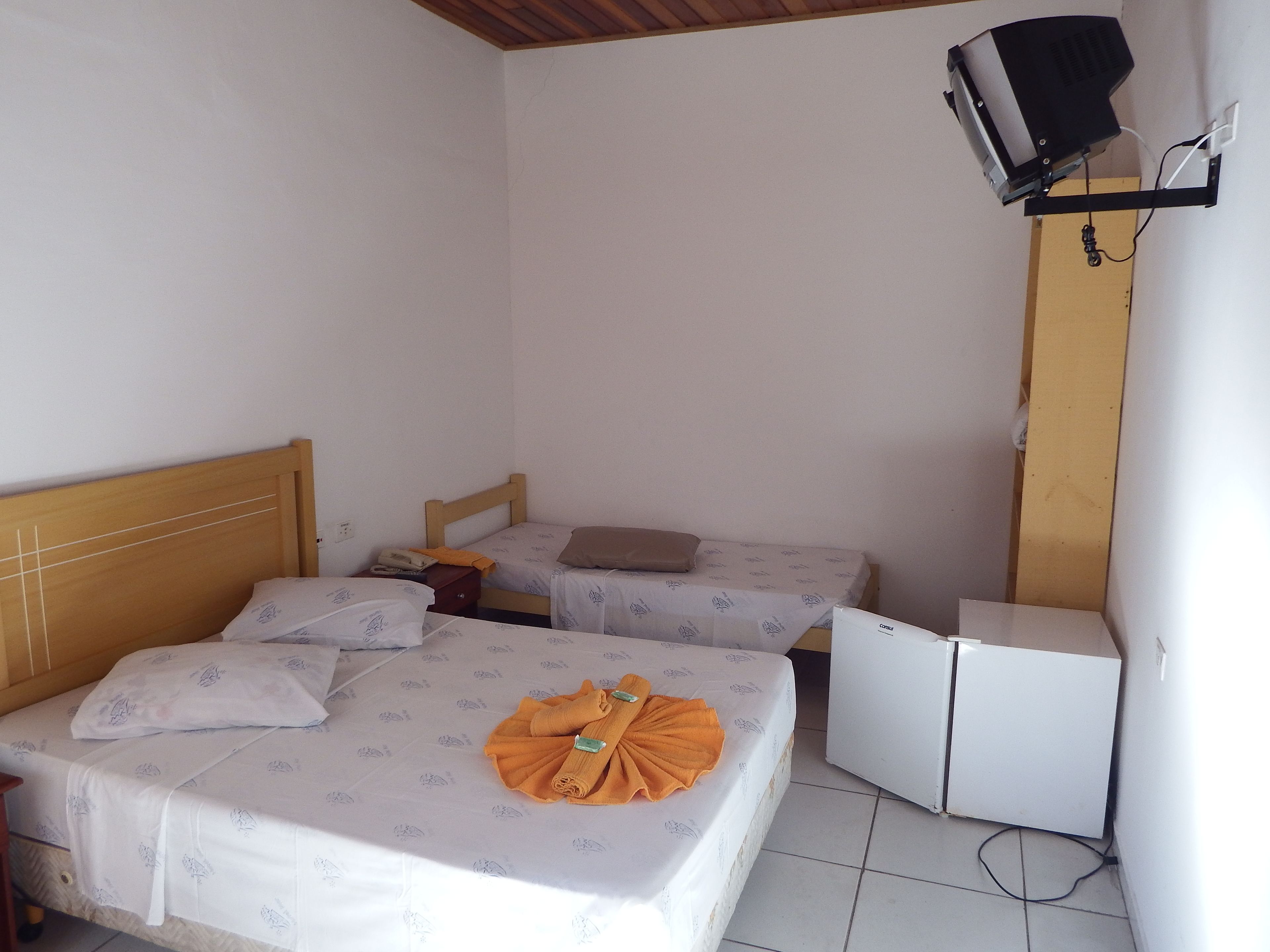 Una habitación pequeña y limpia con dos camas, un escritorio, un televisor y un refrigerador.