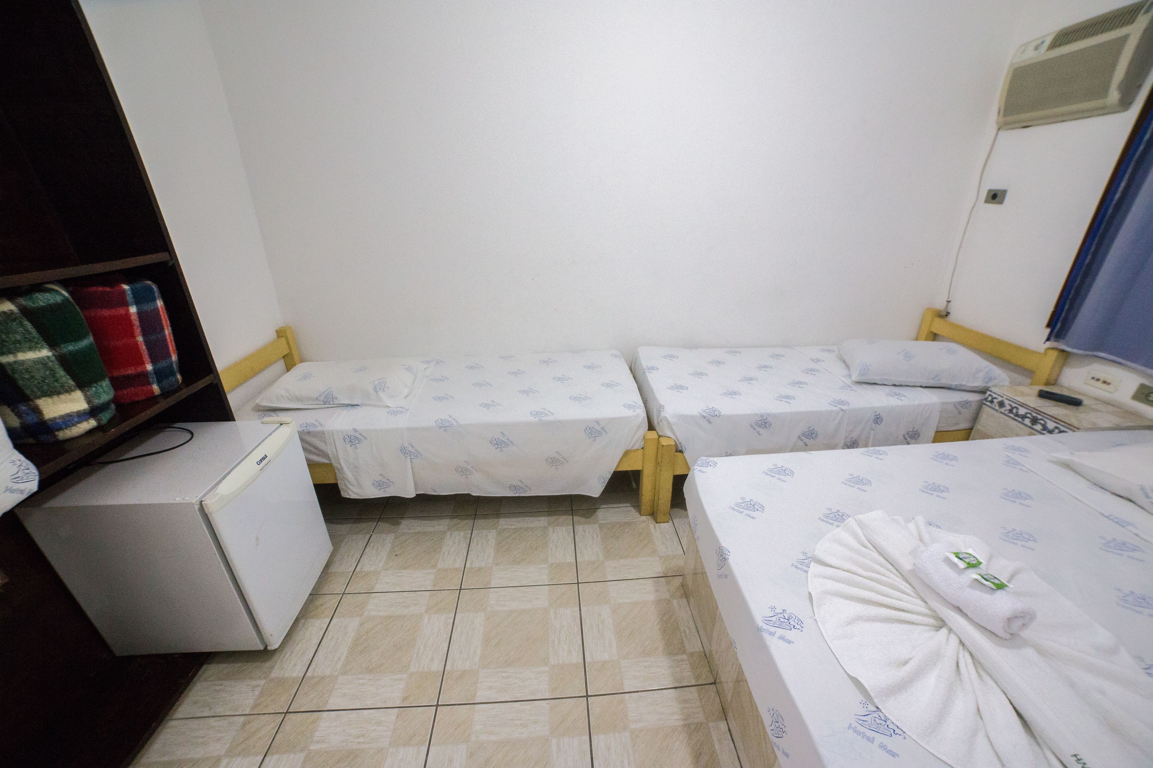 A small, clean room with two single beds, a small refrigerator, and a heater.