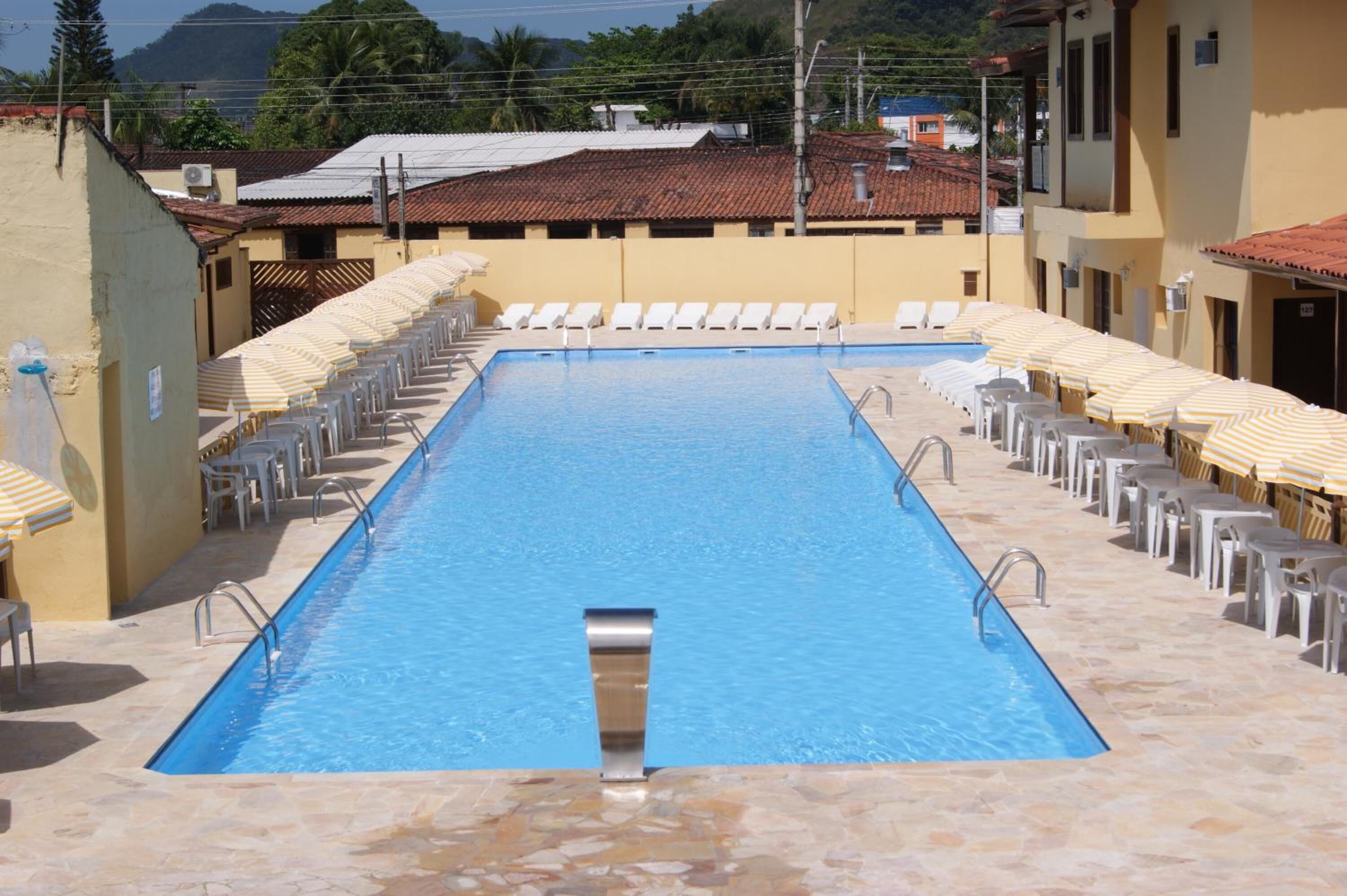 A rectangular swimming pool with clear blue water, surrounded by white lounge chairs and yellow-striped umbrellas.