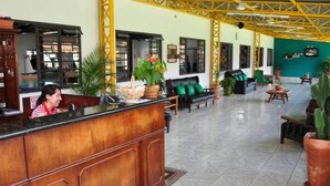 A reception area with a wooden counter, green cushioned seating, and potted plants. - Hotel Fazenda 3 Poderes (Caraguatatuba)