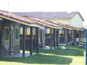 A row of single-story buildings with a tiled roof, outdoor seating, and a grassy area. - Hotel Fazenda 3 Poderes (Caraguatatuba)