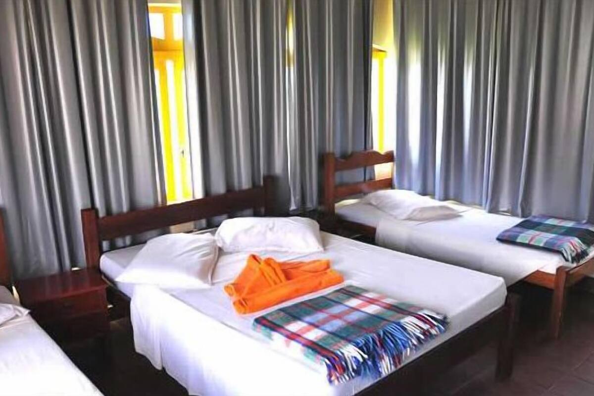 A hotel room with two single beds, wooden headboards, white linens, and a plaid blanket on one bed.