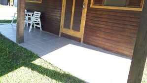 A wooden building with a covered patio area, a table with chairs, and a door with a window. - Hotel Fazenda 3 Poderes (Caraguatatuba)