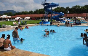 A swimming pool with a water slide, surrounded by umbrellas and people. - Hotel Fazenda 3 Poderes (Caraguatatuba)