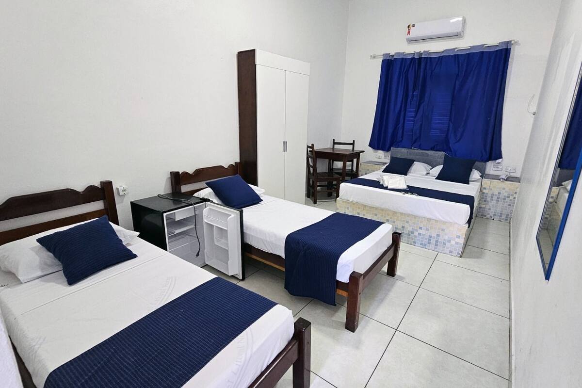 A hotel room with two single beds, a desk with a chair, a small table, and a bathroom with a shower and toilet.