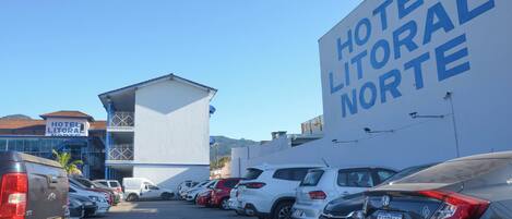 Un estacionamiento de hotel con varios coches aparcados, un edificio con un letrero que dice "HOTEL LITORAL NORTE", y un cielo azul despejado.