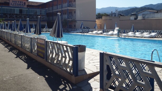 A hotel with a swimming pool, lounge chairs, and umbrellas.