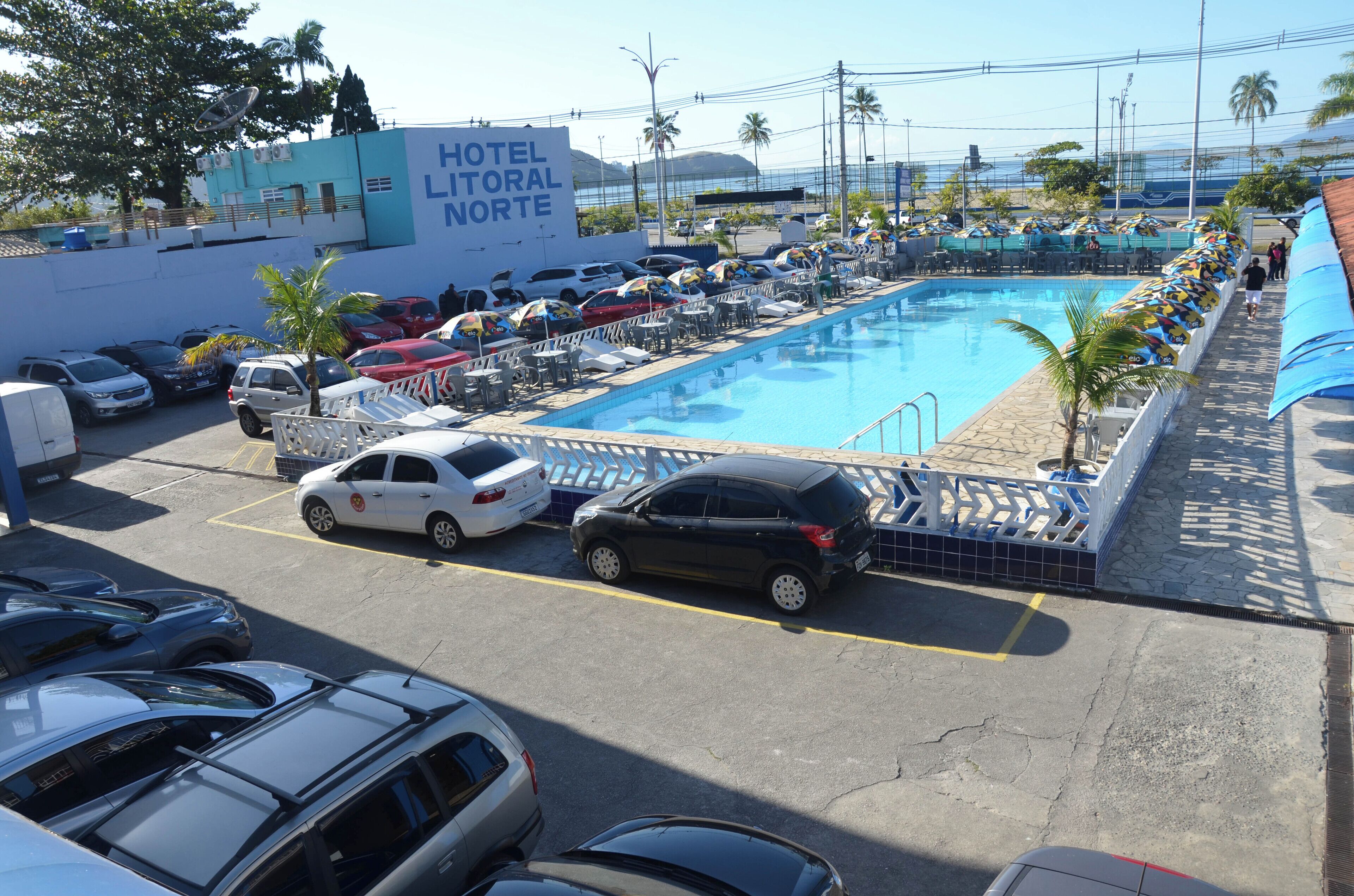 Zona de piscina de hotel con vista despejada, tumbonas y una fila de coches aparcados.