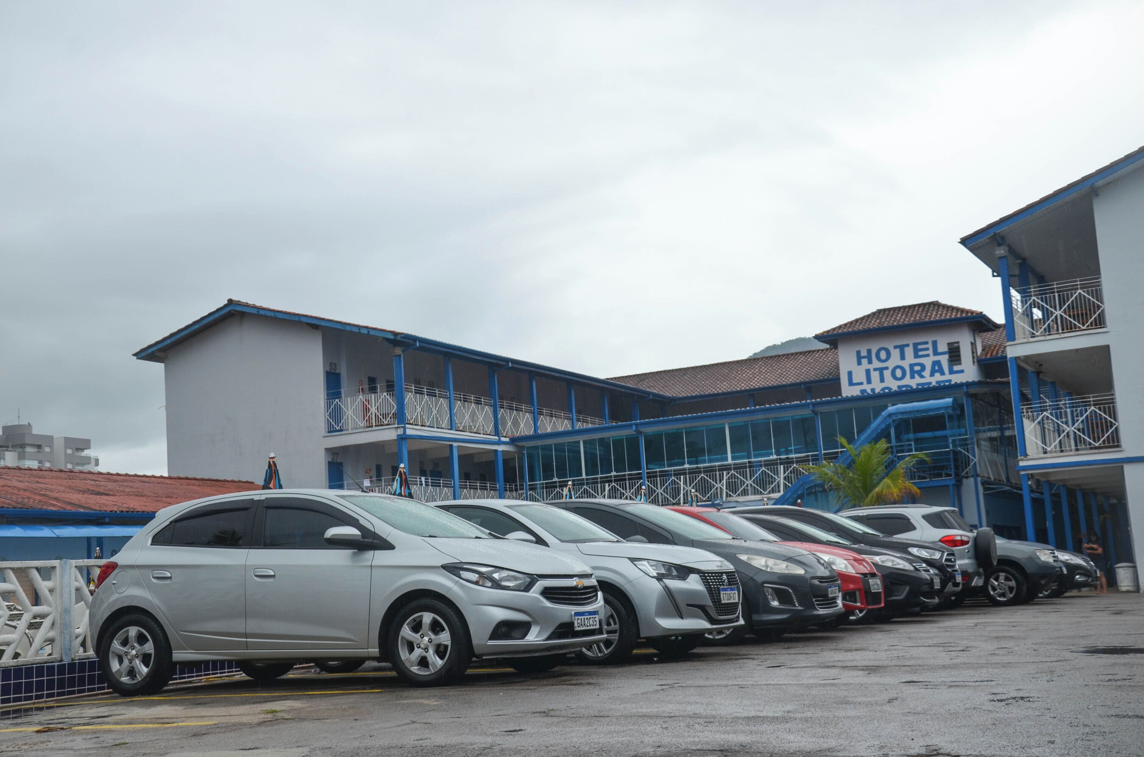 A hotel with a sign reading "HOTEL LITORAL" and a row of parked cars in front.
