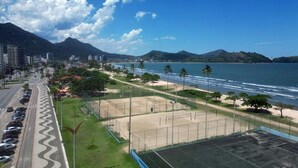A coastal view with a tennis court, beach, and mountains.
