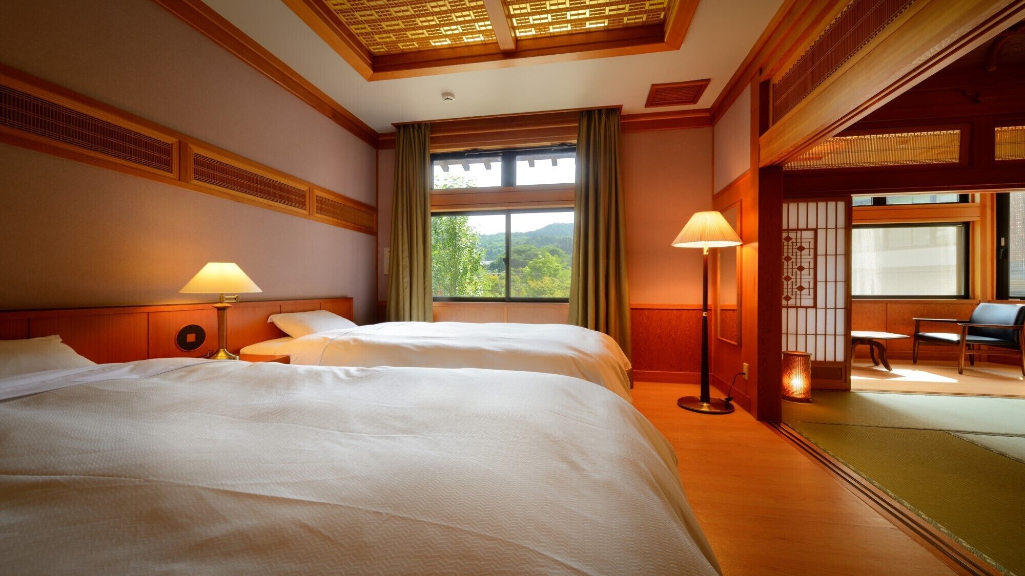 A hotel room with two beds, a large window with a view, a floor lamp, and a seating area with a table and chairs.