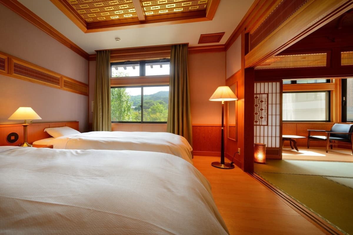 A hotel room with two beds, a large window with a view, a floor lamp, and a seating area with a table and chairs.