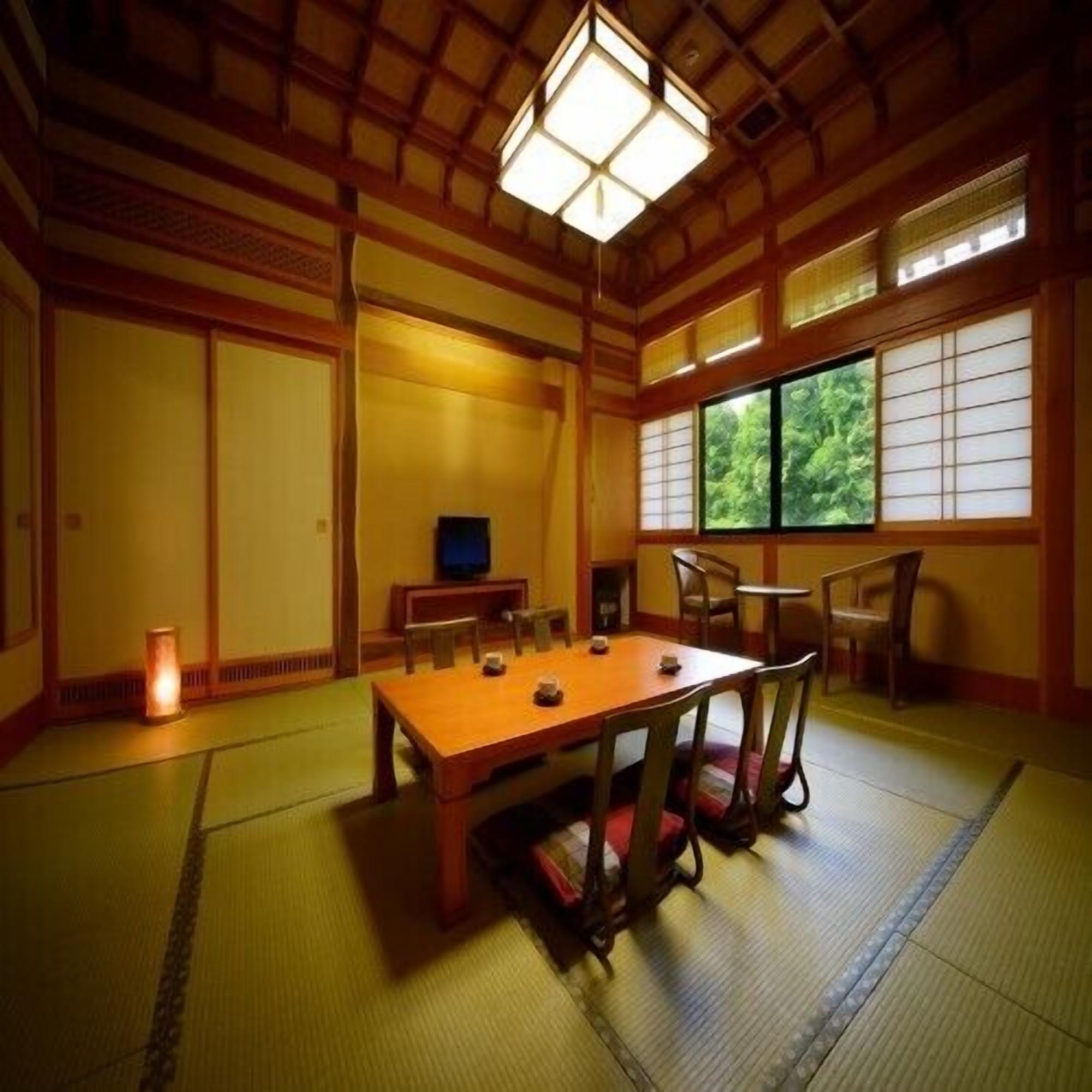 Una habitación tradicional japonesa con suelo de tatami, una mesa baja con sillas, un televisor y un ventanal con puertas shoji.