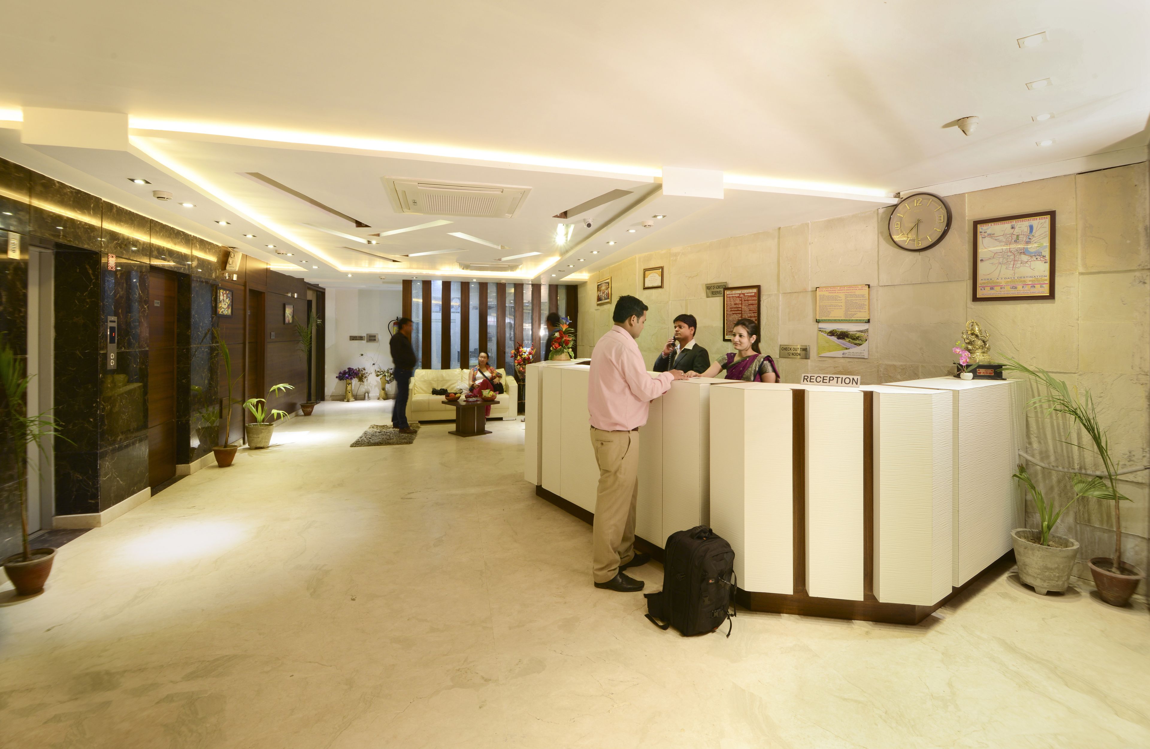 A hotel reception area with a reception desk, a clock, and potted plants.