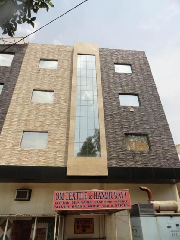 A building with a textured facade, multiple windows, and a sign for 'OM Textile & Handicraft' offering cotton, silk saree, and other items. - Hotel Maniram Palace (Agra)