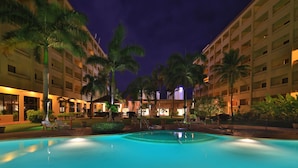 A nighttime view of a hotel pool area with palm trees and a well-lit building facade. - Guam Plaza Resort (Tamuning)