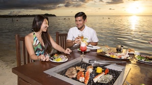 A couple dining at a beachside restaurant with a grill, seafood, and a sunset view. - Guam Plaza Resort (Tamuning)