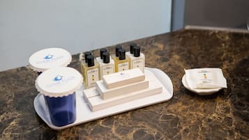 Una bandeja con diversos artículos de tocador, incluyendo una taza azul, varias botellas de champú y una toalla doblada sobre una encimera de mármol.