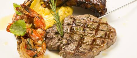 A plate with grilled steak, shrimp, and a sausage, garnished with herbs.