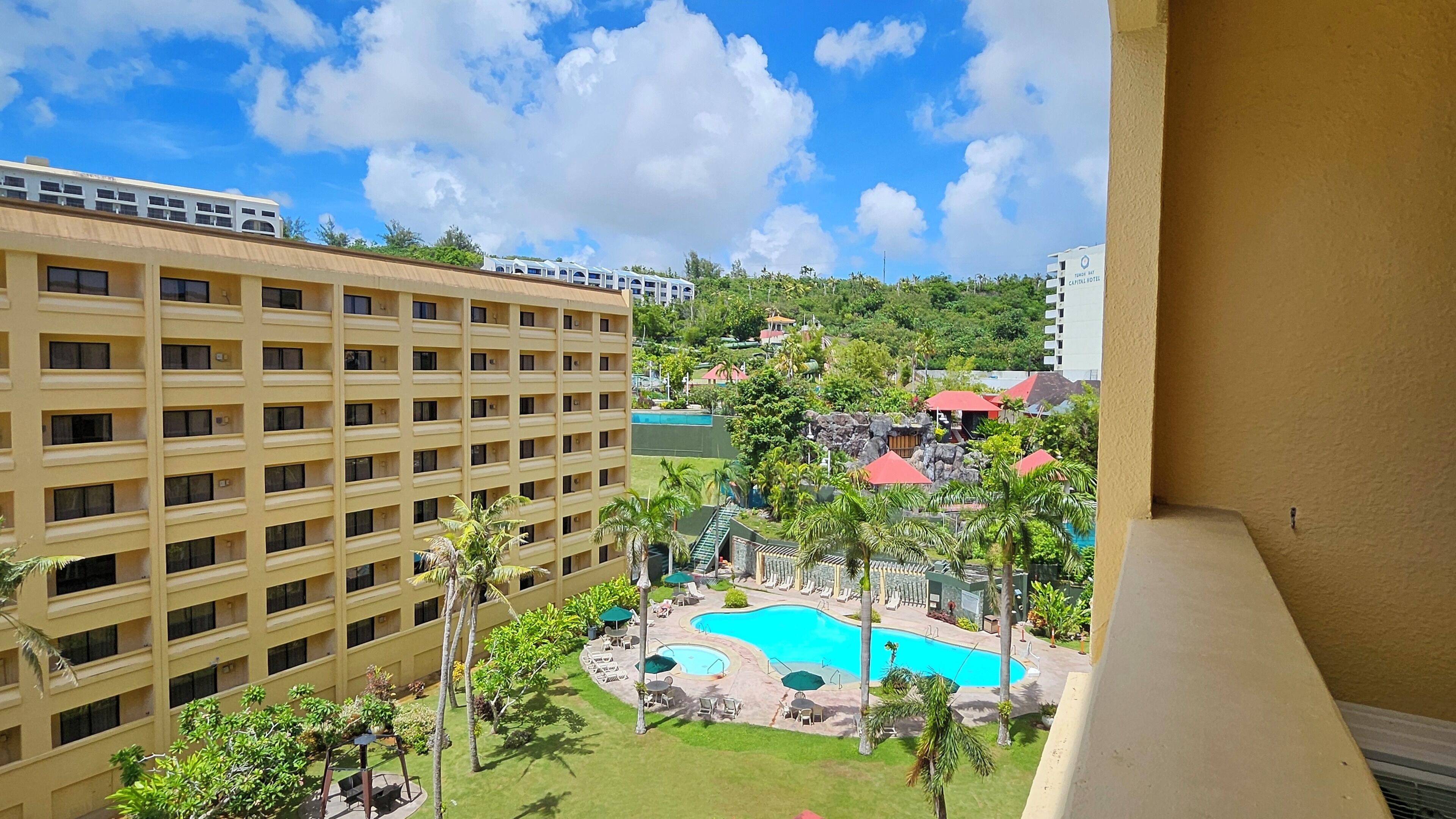 A hotel with multiple floors, a swimming pool, and a lush garden area.