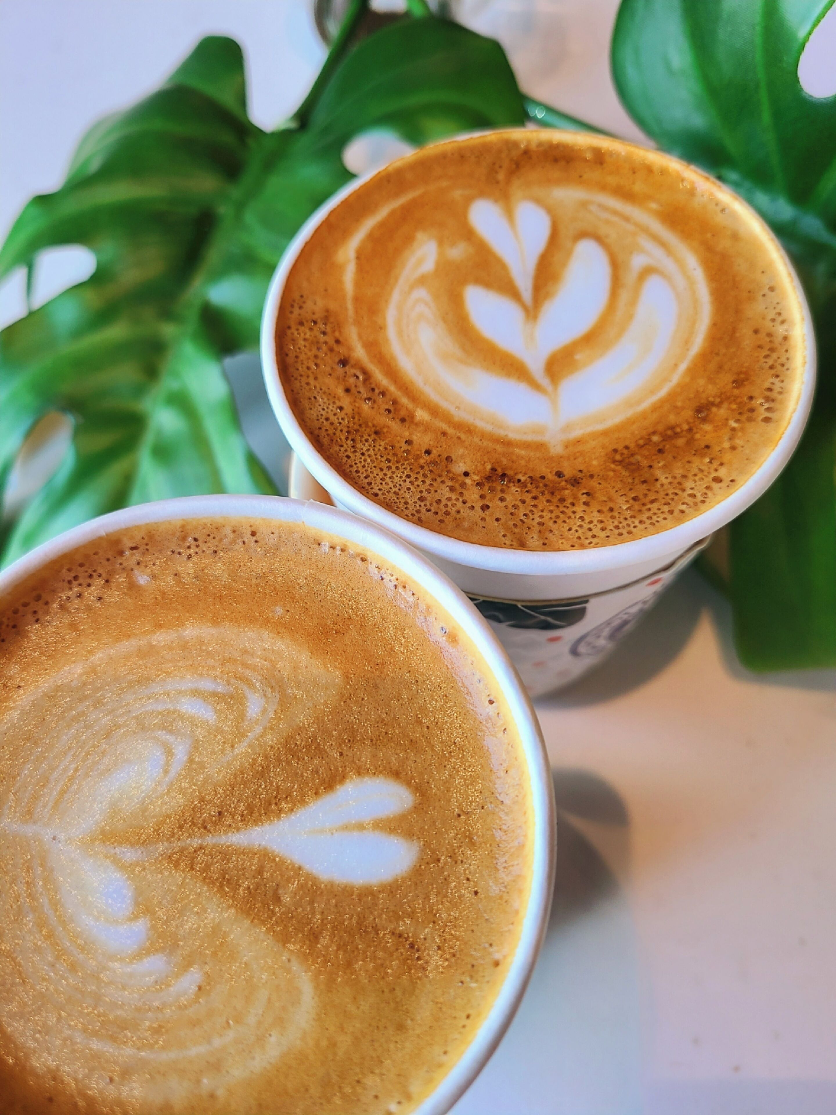 Duas chávenas de café com arte de latte sobre uma superfície branca.