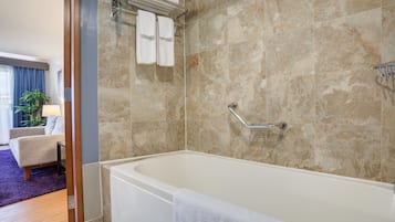 A modern bathroom with a bathtub, a towel rack with towels, and a handrail.