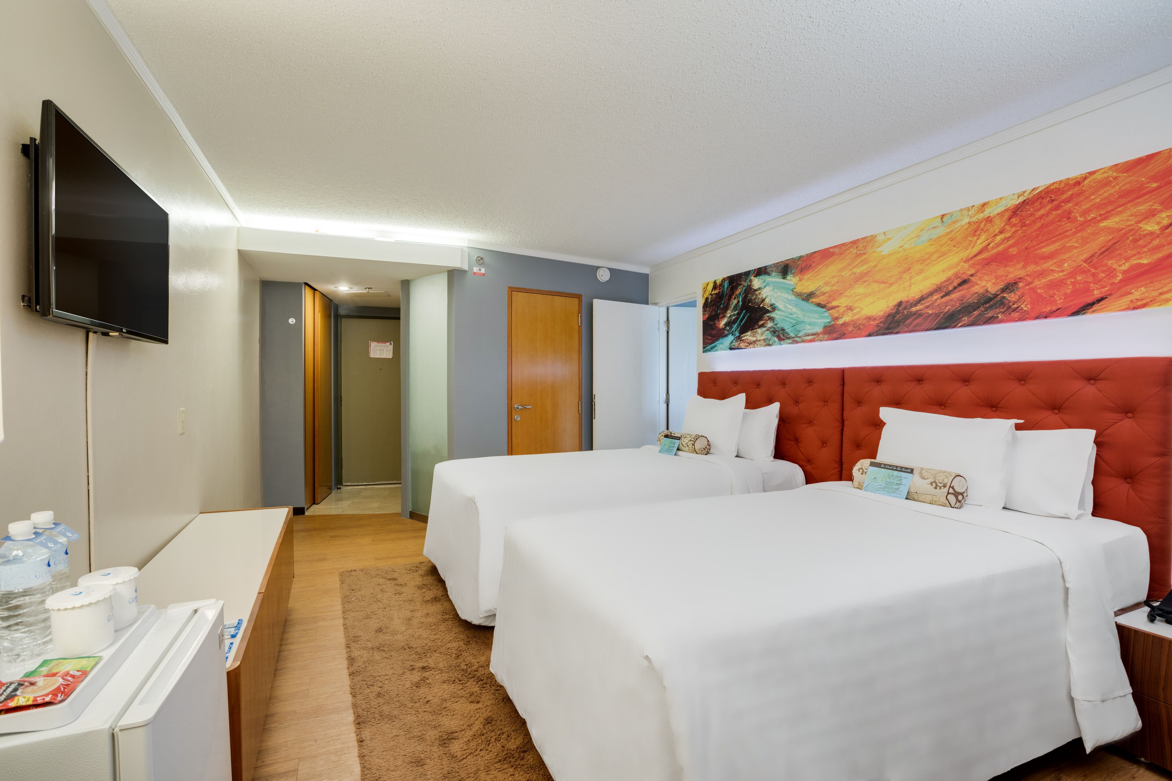 A hotel room with two beds, a TV, a desk, and a large abstract painting on the wall.