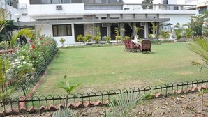A modern two-story house with a covered patio, a lawn, and a garden with various plants. - Pulse Impulse (New Delhi)