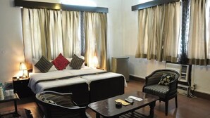 A hotel room with a bed, two chairs, a table, and a nightstand with a lamp. - Pulse Impulse (New Delhi)