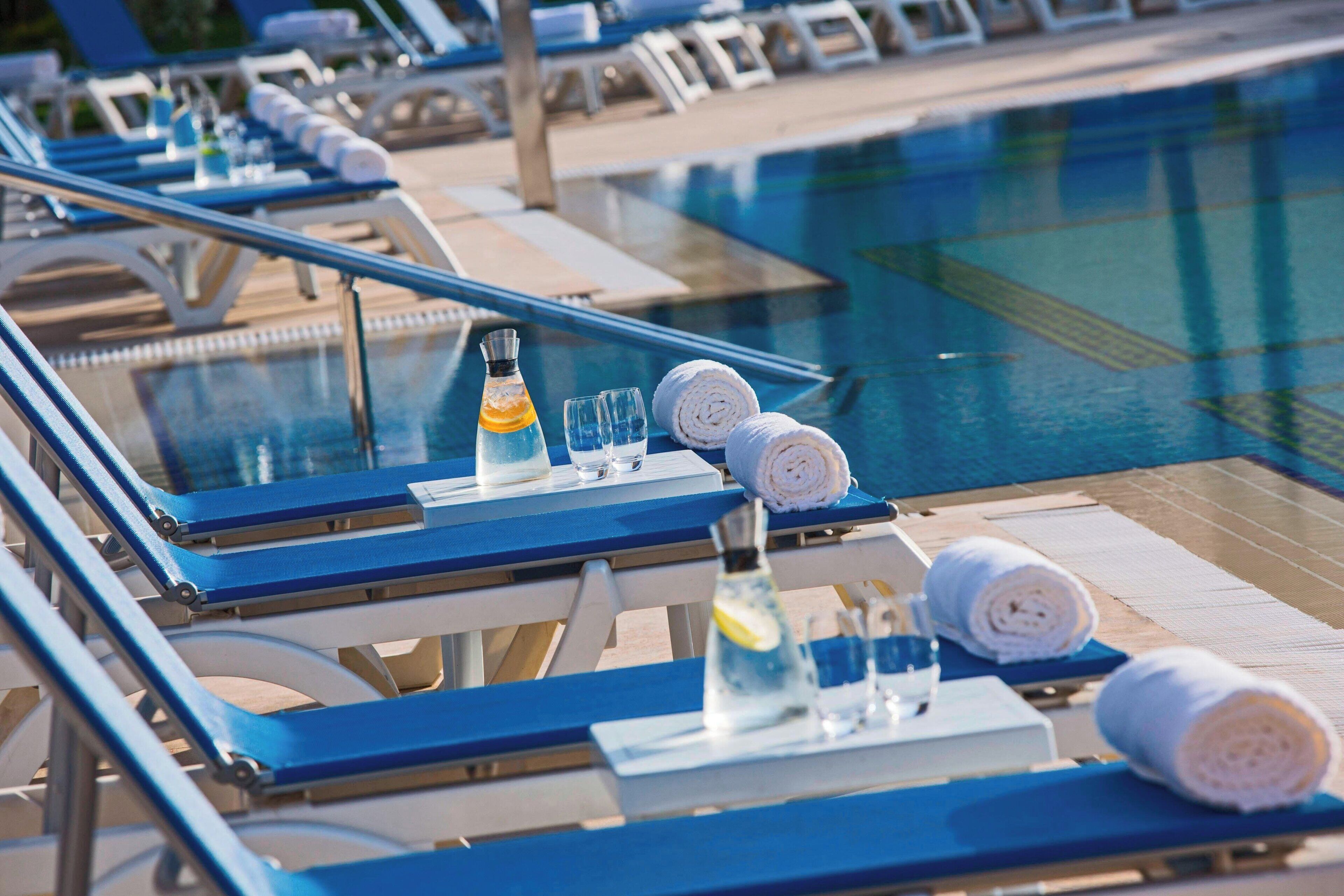 Un espace aménagé au bord de la piscine, avec des chaises longues, une piscine et des équipements tels que des serviettes et une bouteille d’eau.