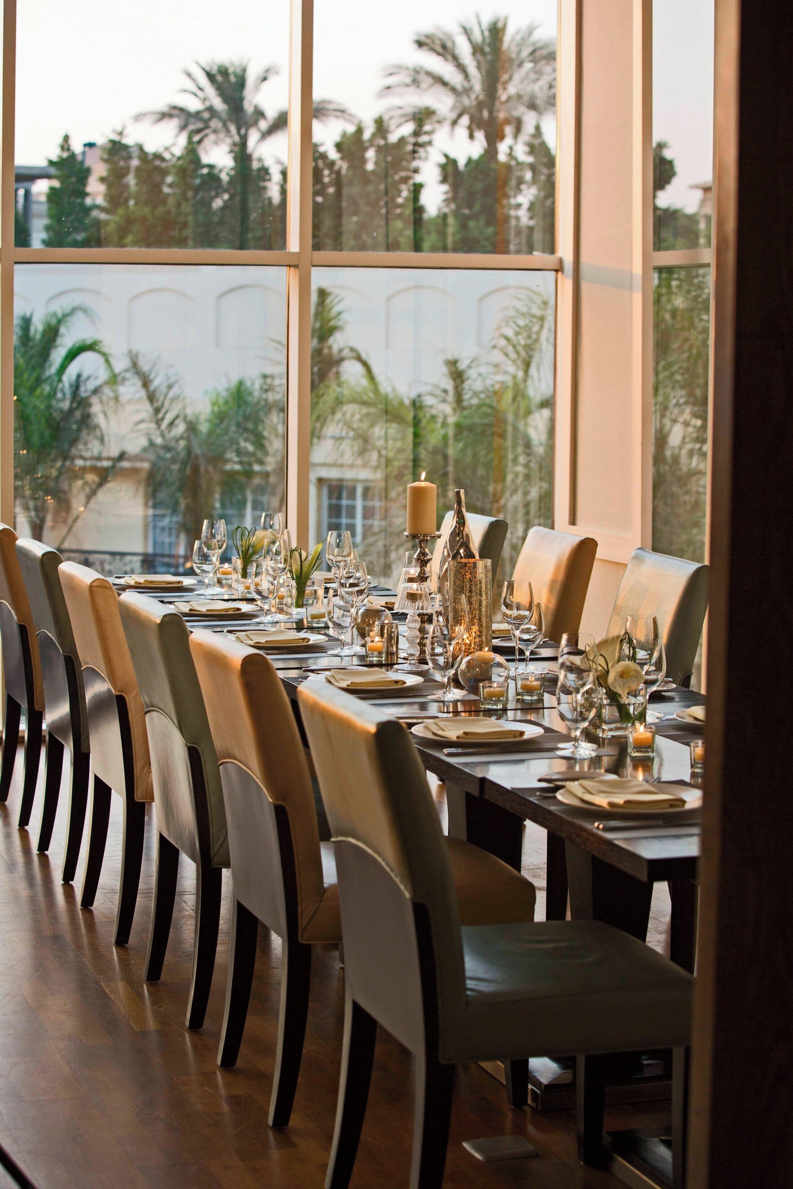 A dining area with a long table set for a meal, large windows, and chairs.