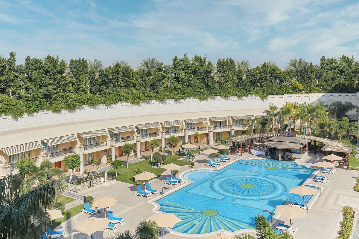 A hotel with a large swimming pool, sun loungers, and a covered area with umbrellas.