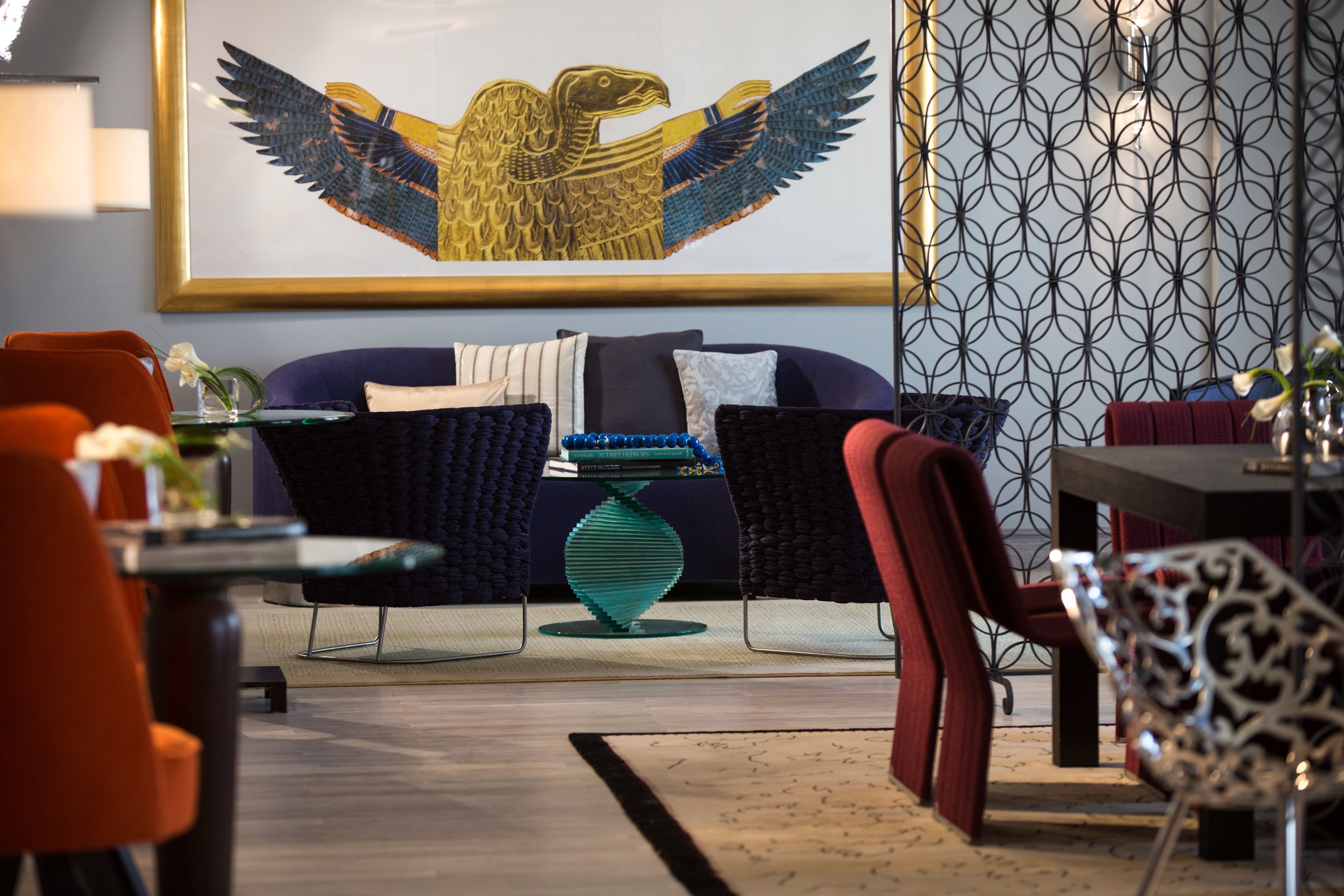 Una sala de estar moderna con un sofá azul, sillas rojas y una mesa de cristal decorativa.