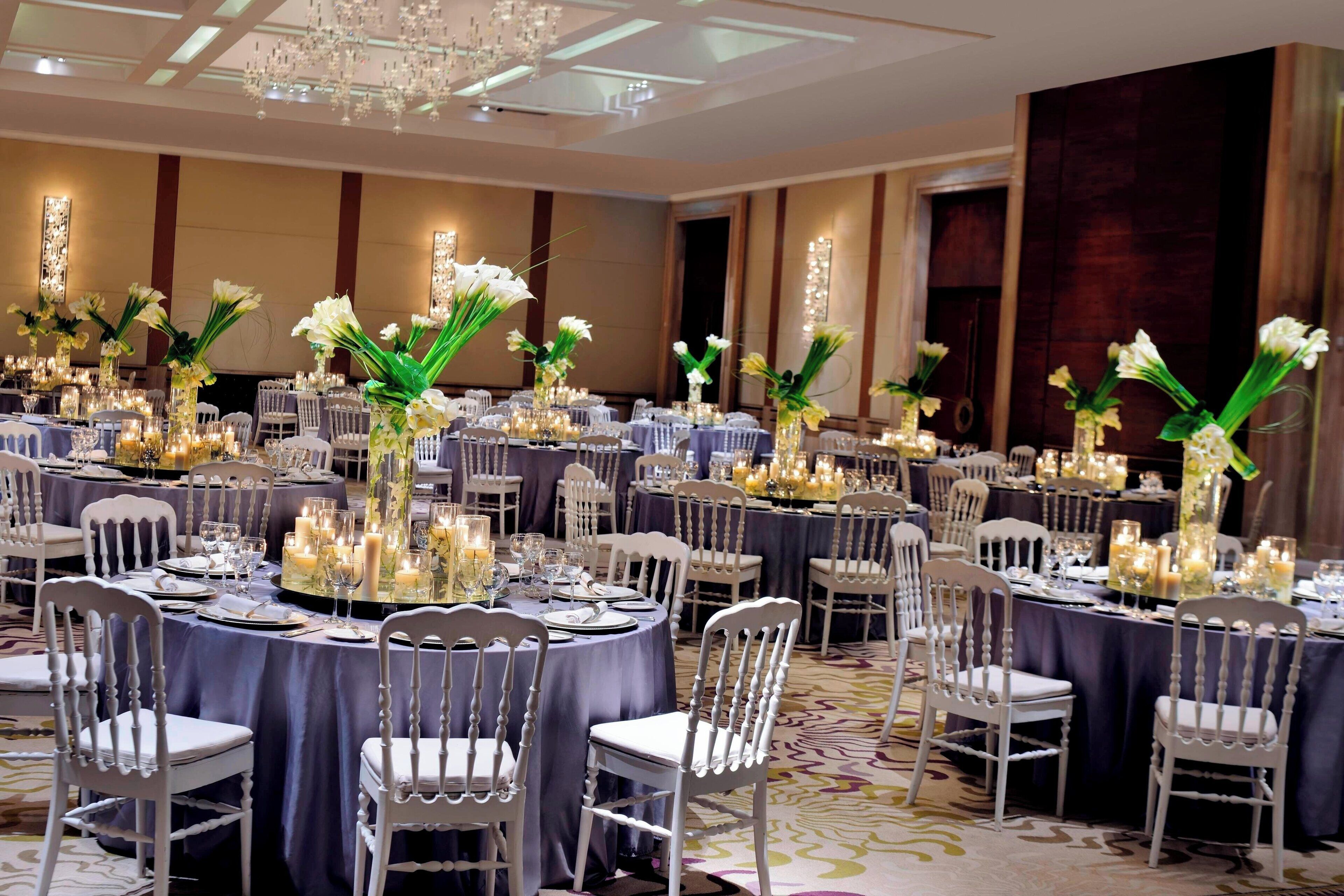 Une salle de banquet avec des tables rondes dressées pour le repas, chacune étant agrémentée de chaises blanches et de compositions florales.