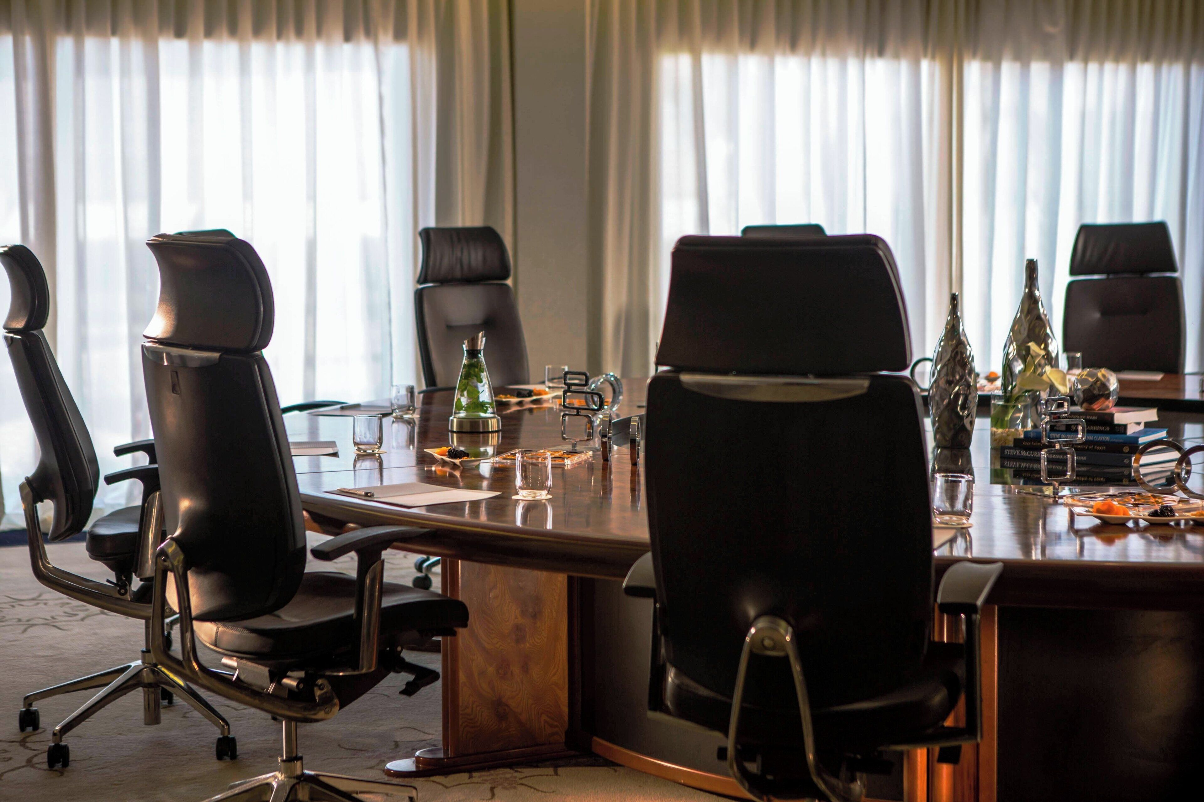 Een vergaderruimte met een lange tafel, vier zwarte stoelen en een glas water op de tafel.