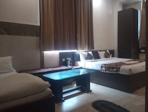 A hotel room with a bed, a sofa, a small table, a wardrobe, and a window with curtains. - Hotel Taj Galaxy  (Agra)