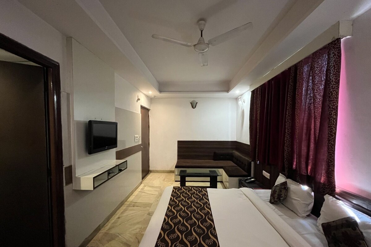 A hotel room with a bed, a television mounted on the wall, a ceiling fan, and a window with curtains.