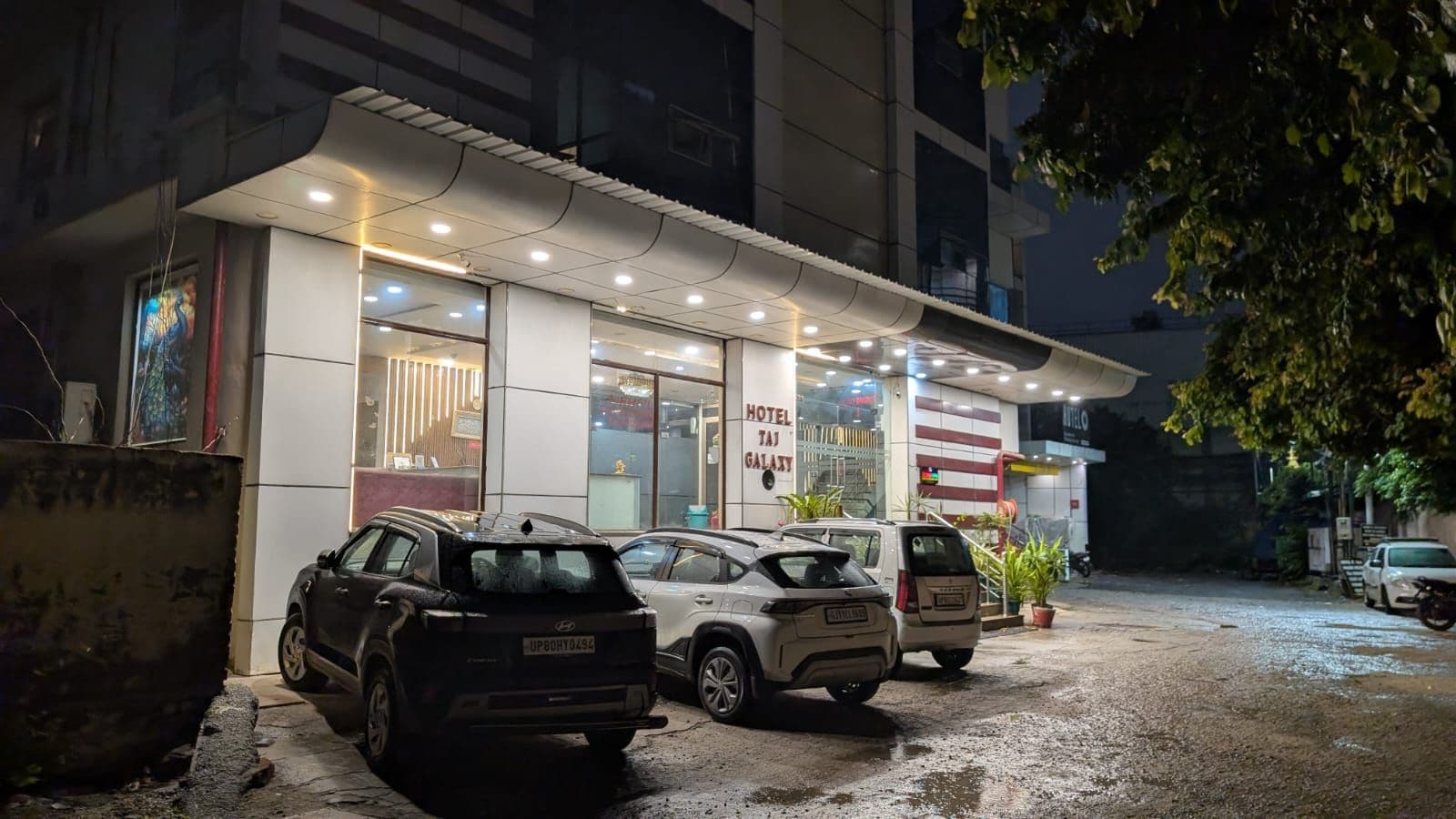 A hotel with a modern facade, multiple parked cars, and a sign indicating the name 'HOTEL TAI GALLERY'.