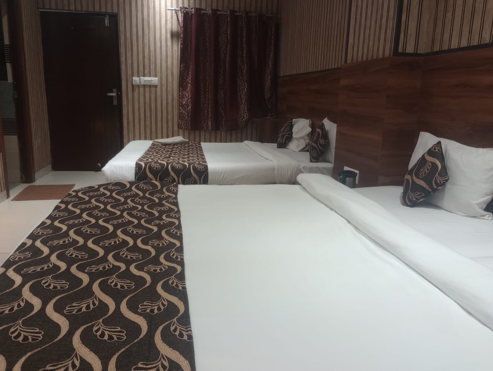 A hotel room with two beds, a patterned carpet, and a wooden headboard.