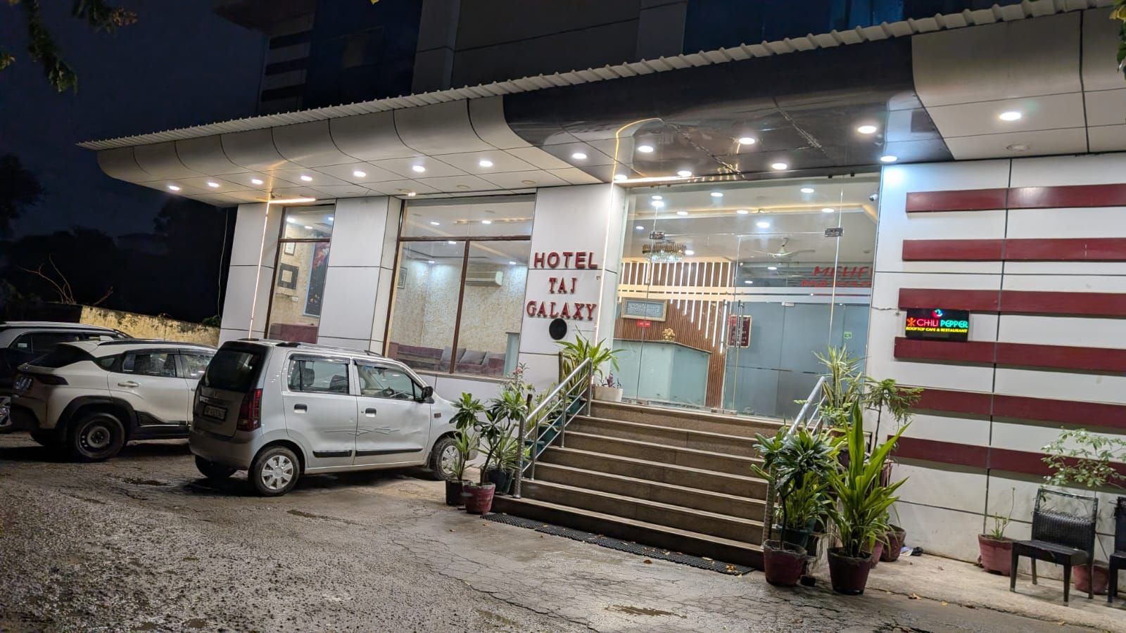 A hotel entrance with a sign reading 'HOTEL TAI GALAXY,' a staircase leading to the entrance, and a parked car.