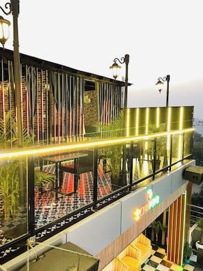 A multi-level building with a glass railing, outdoor seating, and a neon sign. - Hotel Taj Galaxy  (Agra)