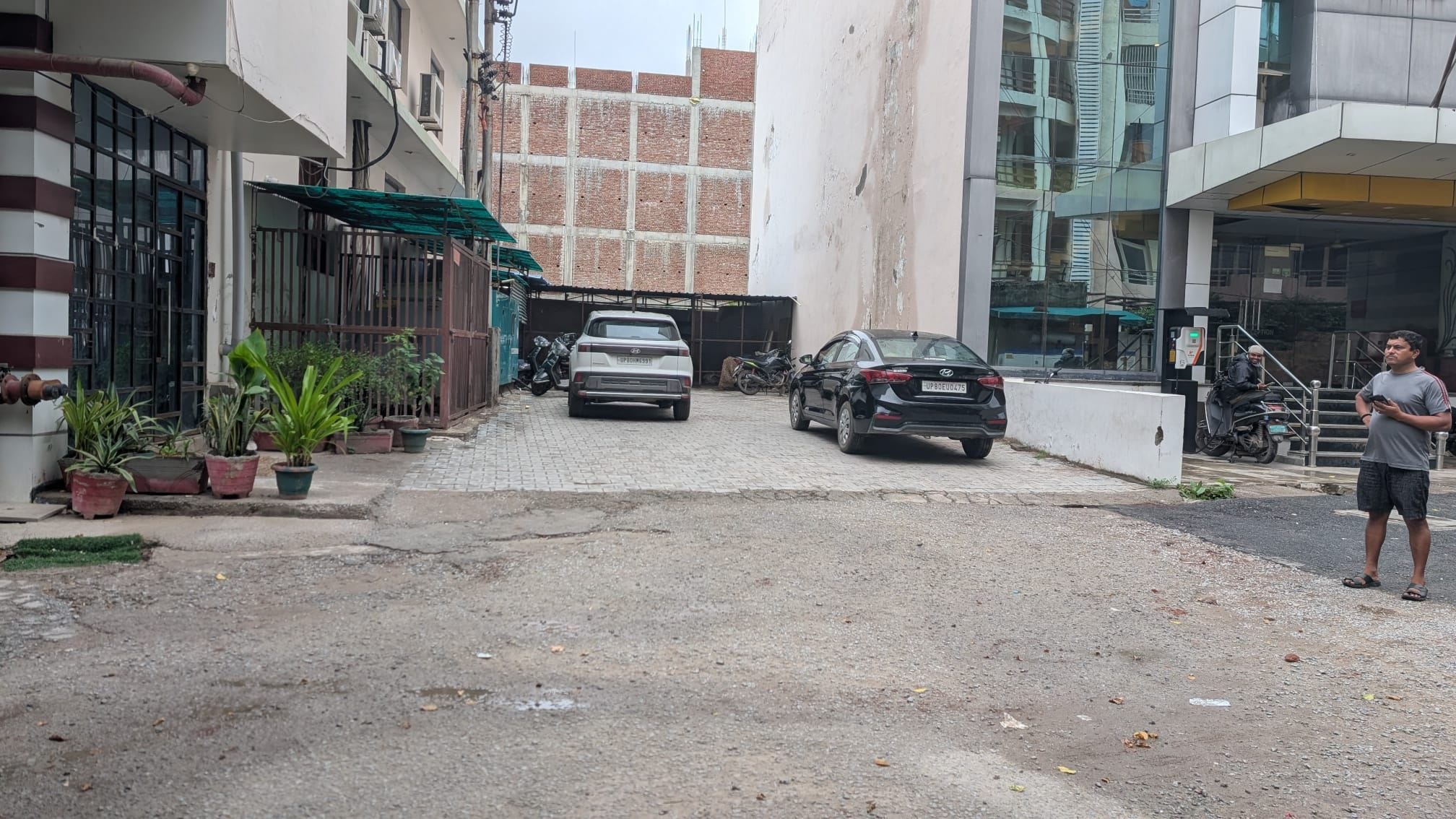 A narrow street with parked cars and potted plants on the side.
