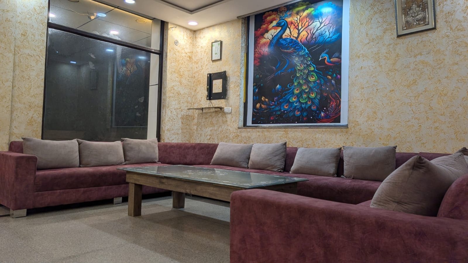 A room with a large sofa set and a coffee table, a large window, and a colorful peacock painting on the wall.