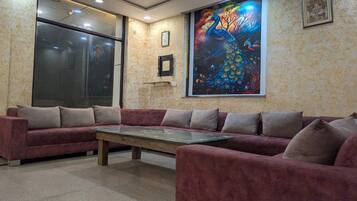 A room with a large sofa set and a coffee table, a large window, and a colorful peacock painting on the wall.
