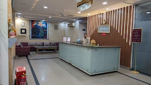 A hotel reception area with a reception desk, a sofa, a bench, and a wall-mounted air conditioning unit. - Hotel Taj Galaxy (Agra)