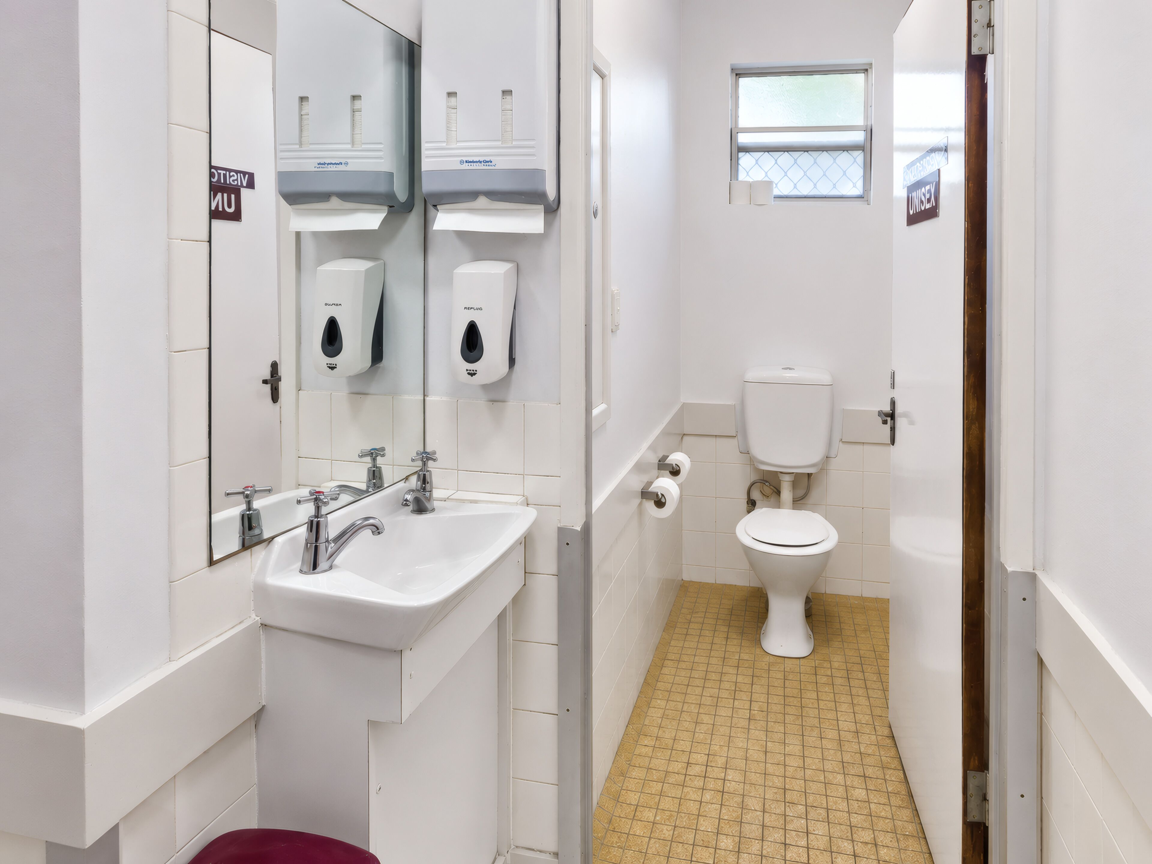 Une salle de bain propre et moderne, équipée d’un lavabo, d’un miroir, de toilettes et de distributeurs de gel hydroalcoolique.