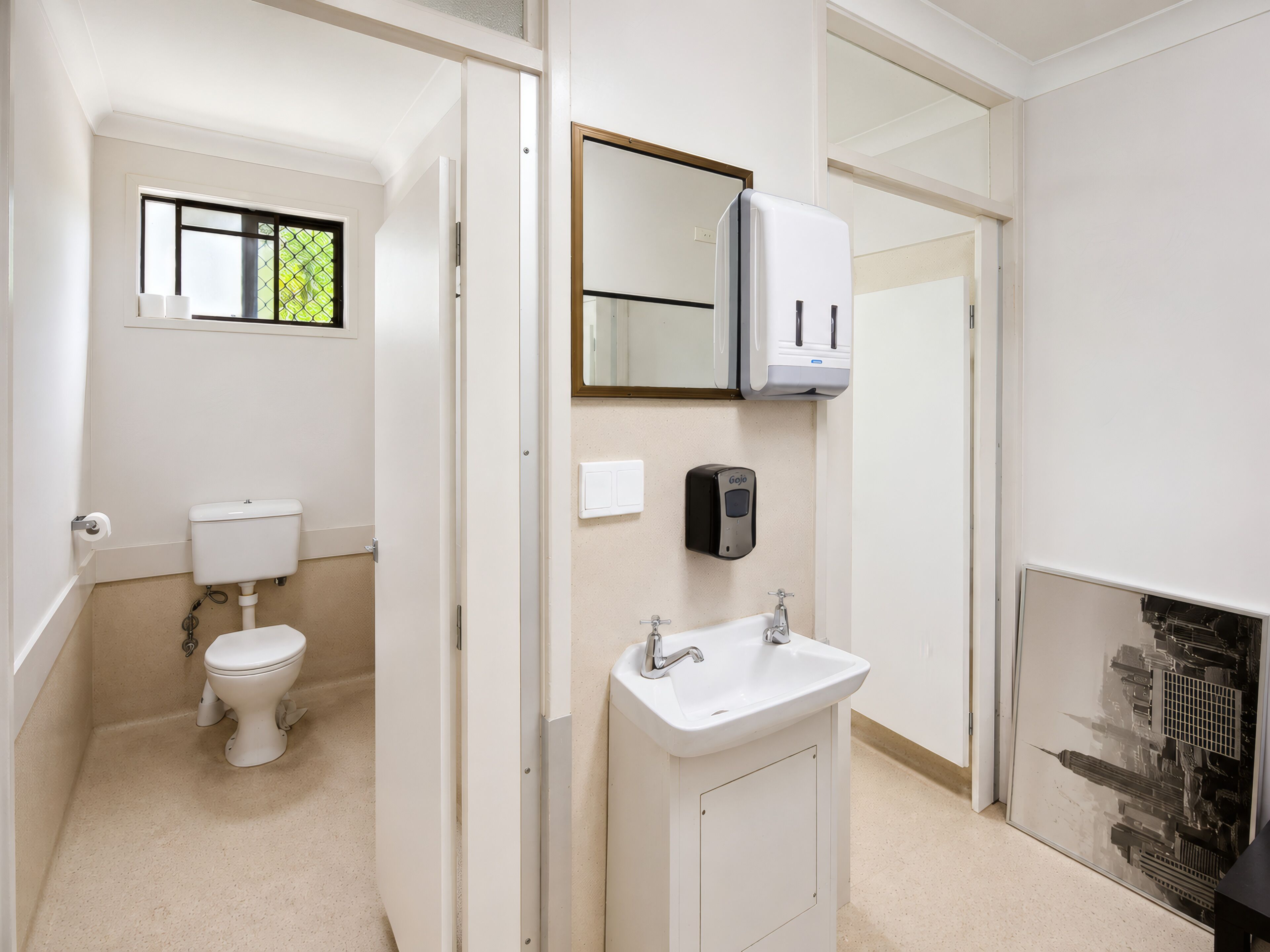 Baño con inodoro, lavabo, espejo y dispensador de desinfectante de manos.
