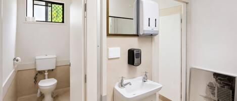 Baño con inodoro, lavabo, espejo y dispensador de desinfectante de manos.